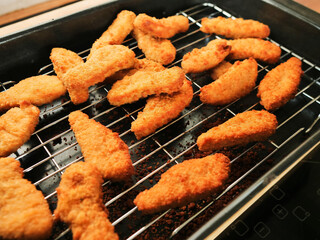 A rack of chicken goujons are on a metal cooking tray. The nuggets are golden brown and crispy. Simple tasty family meal. Cooking meat. concept