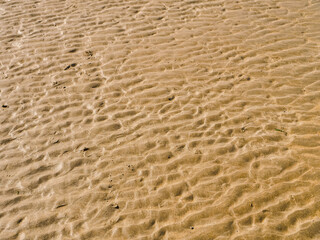 The sand is brown and has a lot of texture. It looks like it has been disturbed by the wind