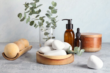 Wooden bowl with spa stones and eucalyptus twig on blue grunge background