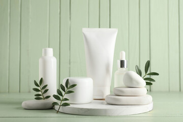 Composition with spa stones, green leaves, jar and bottles of cosmetic products on green wooden background, closeup
