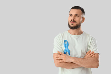 Young man with blue ribbon on light background. Prostate cancer awareness concept