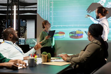 Diverse group of corporate associates look into project timelines and agenda, creating a strategy for development after hours in conference room. Goal setting in a business environment.
