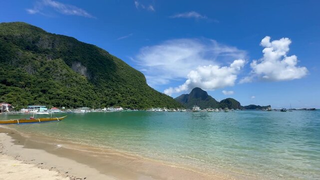 View of El Nido port from the beach with traditional bancas anchored. Iconic destination for tourism, diving, and island hopping in Southeast Asia.