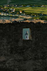 Scenic view through stone window of ruined castle, focusing on blue baroque church with sunlit vineyards in background on a bright summer day in Austria.