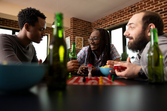 African american individuals and caucasian man having conversation during board game session. Multiethnic group of friends seated with snacks and drinks around table, bonding with each other.