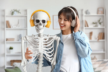 Young woman with human skeleton model in headphones at home