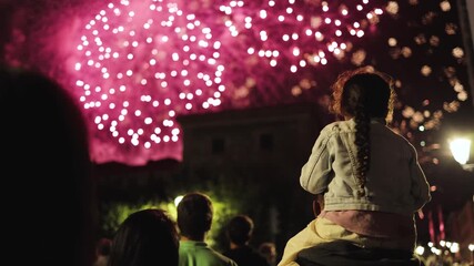 A little girl sits on her parent’s shoulders, watching dazzling fireworks illuminate the night sky. Magical festive atmosphere, childhood wonder, New Year, Christmas, holiday, festival, amazing - Powered by Adobe