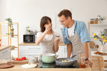 Young couple tasting soup in kitchen