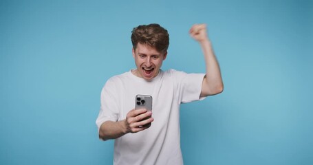 Excited man celebrates success while holding smartphone in bright blue room