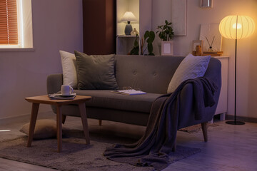 Obraz premium Interior of dark living room with sofa, table and glowing lamps in evening