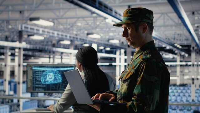 Military soldier and engineer in server room use AI tools to manage computer systems. Army commander and female programmer review information using artificial intelligence in server farm, camera B