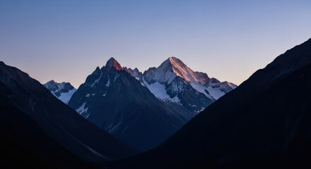 Sunset illuminating snow-capped mountain peaks amidst shadowed valleys in tranquil twilight