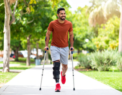 Smiling Man with Prosthetic Leg Walks Confidently on Pathway, Sunny Day.