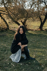 a portrait of a brunette girl dressed in a light dress and a knitted sweater walking in the countryside