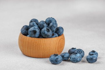 Fresh ripe blueberries in small wooden bowl on gray textured stone background. Delicious organic fruit rich in vitamins, wild berries,healthy lifestyle, natural food. Close up, macro