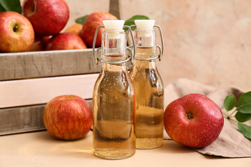 Bottles of fresh apple cider and wooden box with fruits on beige background