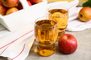 Glasses of fresh apple cider and fruits on grey background