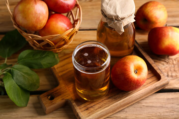 Bottle and glass of fresh apple cider with fruits on wooden background, closeup