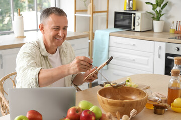 Mature man with recipe book and apple cider at table in kitchen