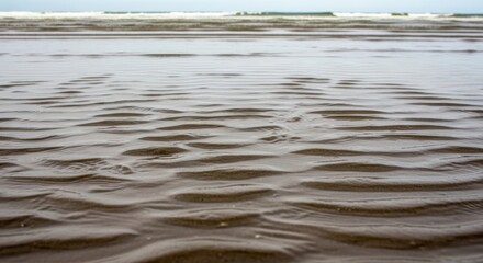 Rippled sand beach at low tide with gentle waves in the background