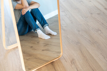 Reflection in mirrow of a sad woman sitting on a floor alone in empty room, despair and lonely...