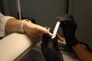 A skilled manicurist in black gloves files and shapes a client's nails, focusing on precision and care during a manicure session