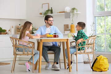Obraz premium Happy father with his children drinking tea at table in kitchen