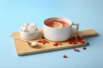 Cup of hot goji tea with lemon and cubes of sugar on blue background