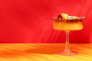 Glass of tasty Mai Tai cocktail garnished with lime and pineapple on orange table against red background
