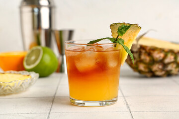 Glass of tasty Mai Tai cocktail with pineapple and mint on white tile table