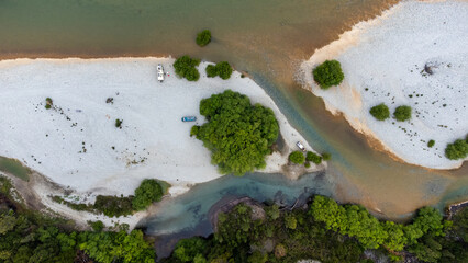 An aerial view reveals three camper vans parked on a remote gravel river bar. Friends enjoying the freedom of overlanding and van life in stunning Patagonian wilderness