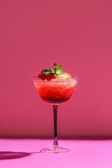 Glass of tasty Mai Tai cocktail garnished with cherries and lime on pink background