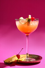 Glass of tasty Mai Tai cocktail garnished with lime and pineapple on pink background