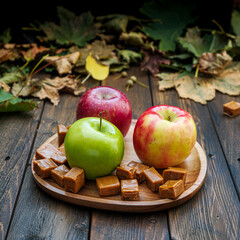 Fall wood plank table with apples and caramel on brown wooden plate with autumn leaves