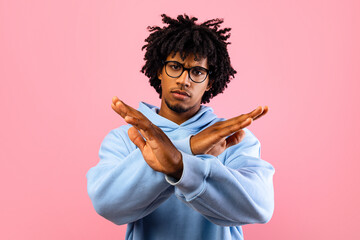 Displeased black teenager gesturing STOP, expressing his disagreement on pink studio background. Assertive African American teen saying NO, showing rejection gesture, refusing something
