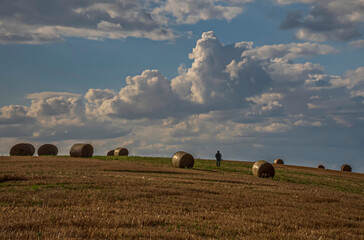 On the field, hay bales line the landscape, with the silhouette of a walking person completing the rural autumn scenery.