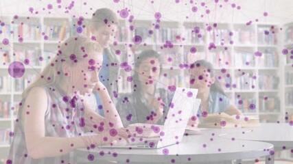 Students rising behind classmate, initiating group assignment in library using laptop and notebook