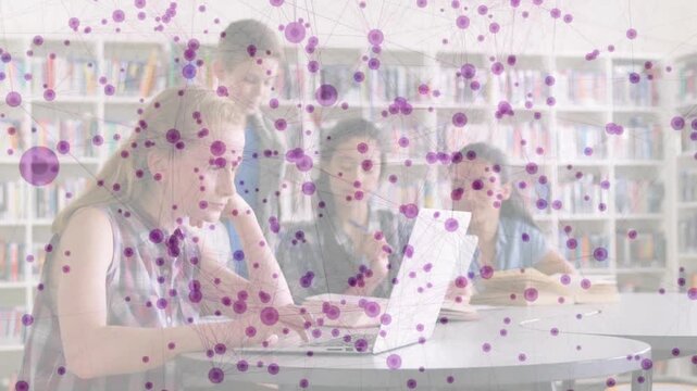 Students rising behind classmate, initiating group assignment in library using laptop and notebook