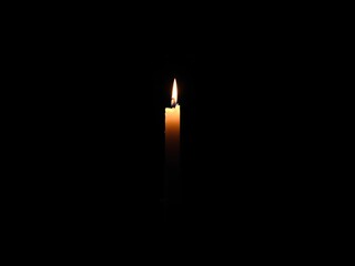 Fototapeta premium A solitary candle's yellow flame burns brightly in the deep blackness, its gentle glow a beacon of warmth and light
