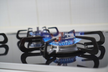 Close-up of a household gas stove burner with visible blue flame burning, modern cooking equipment for home kitchen interior