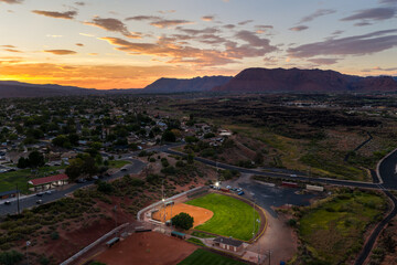 Aerial view of a baseball field at sunset in a small town surrounded by desert landscape, neighborhoods, and mountains in the distance. © Samuel