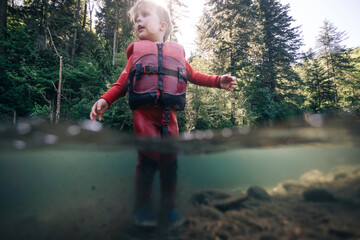 A toddler enjoys walking in the water of a clear river in the Pacific Northwest.