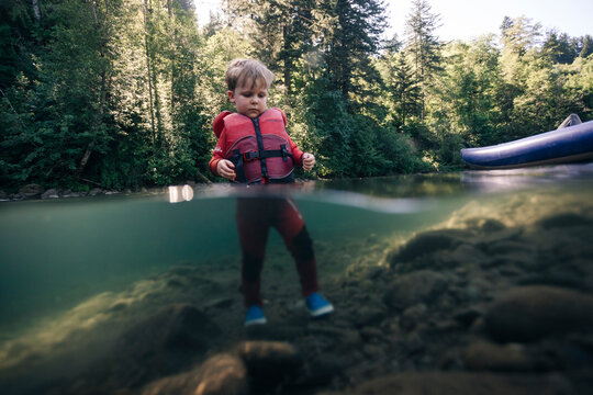 A toddler enjoys walking in the water of a clear river in the Pacific Northwest.