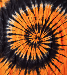 Close-up tie-dye fabric, vibrant orange and black swirling pattern