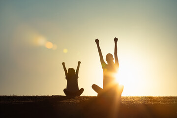joyful parent and child in silhouette during a golden hour sunset, their arms raised in an expressive outdoor setting symbolizing togetherness, happiness, family victory and unity .  © kieferpix