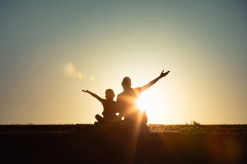 Fototapeta premium joyful parent and child in silhouette during a golden hour sunset, their arms raised in an expressive outdoor setting symbolizing togetherness, happiness, and family unity, hope 