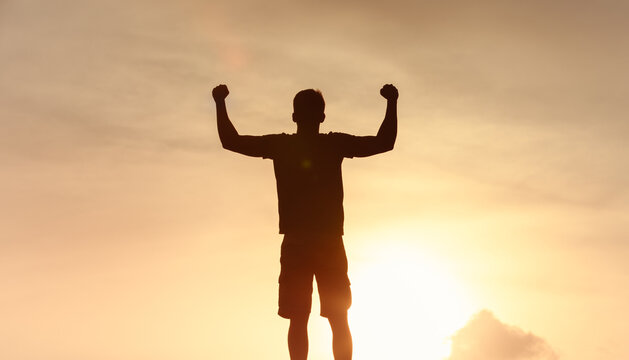 silhouetted man stands with arms raised, showcasing triumph and freedom