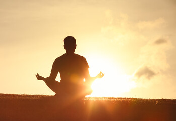 Silhouette of a man meditating on a grassy field with a golden sunset backdrop, evoking relaxation, mindfulness, and inner peace tranquility, spirituality, and connection with nature 