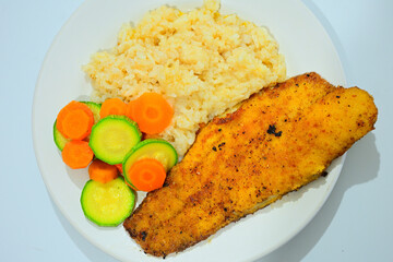 A delicious and colorful plate featuring a seasoned fish fillet, served with fluffy rice and a side of sliced carrots and zucchini, perfect for healthy eating, home cooking, and nutrition themes