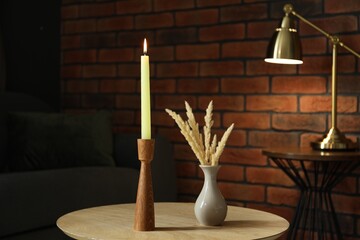 Burning candle and vase with spikelets on wooden table at home